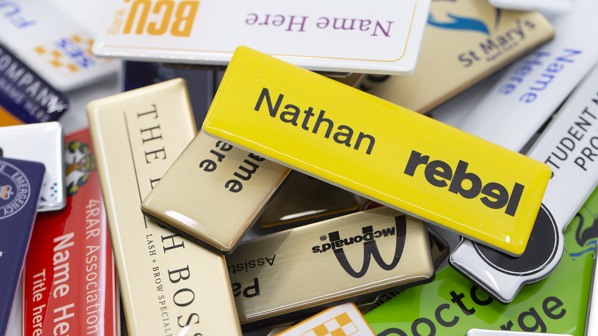 Assorted magnetic name badges in different colours and designs, with a yellow Nathan Rebel badge on top.