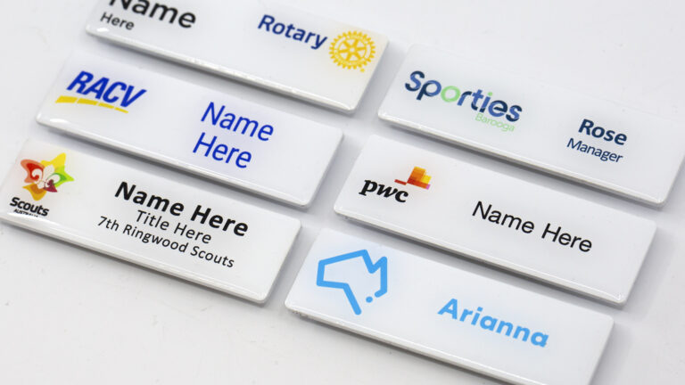 Close-up view of white magnetic name badges showing different logo designs and placeholder names.